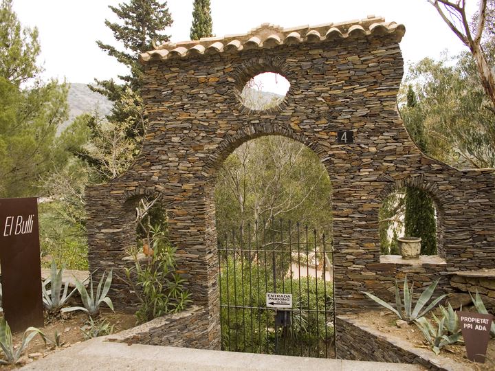 A rough stone arch and gate leading into the gardens of the former El Bulli restaurant