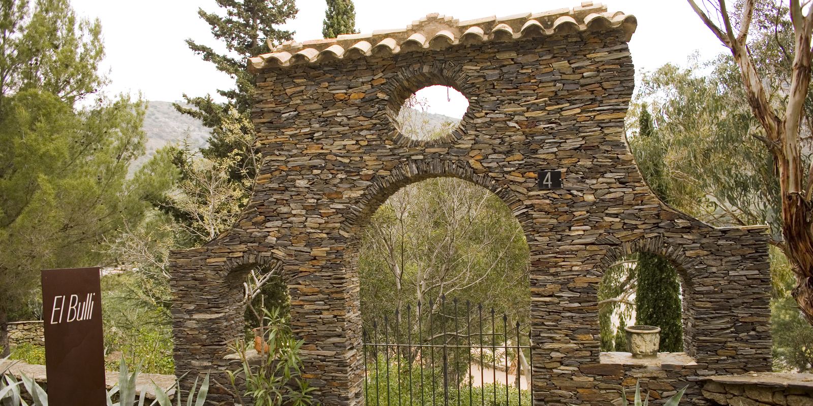 A rough stone arch and gate leading into the gardens of the former El Bulli restaurant