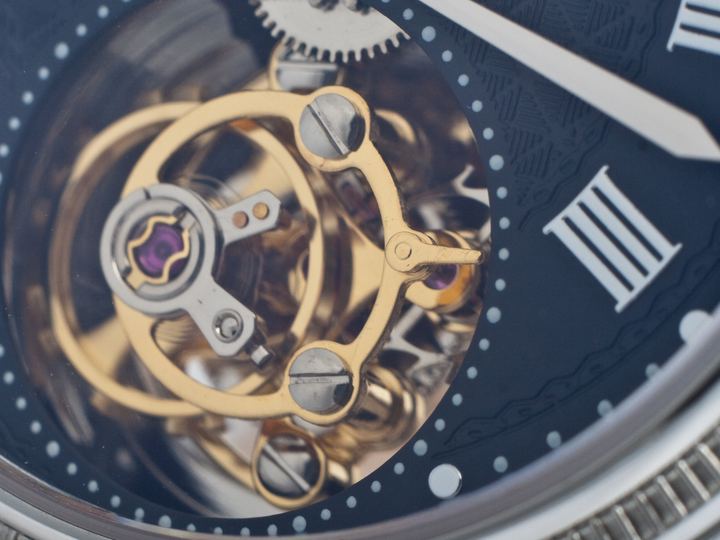 Close-up of a tourbillon cage with a gold balance wheel visible through a watch dial