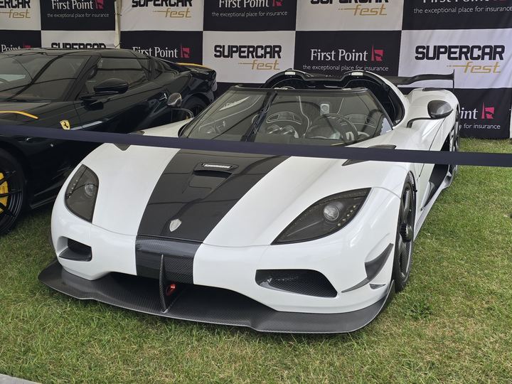 A white Koenigsegg Agera RS with a black stripe and roof scoop at a car show