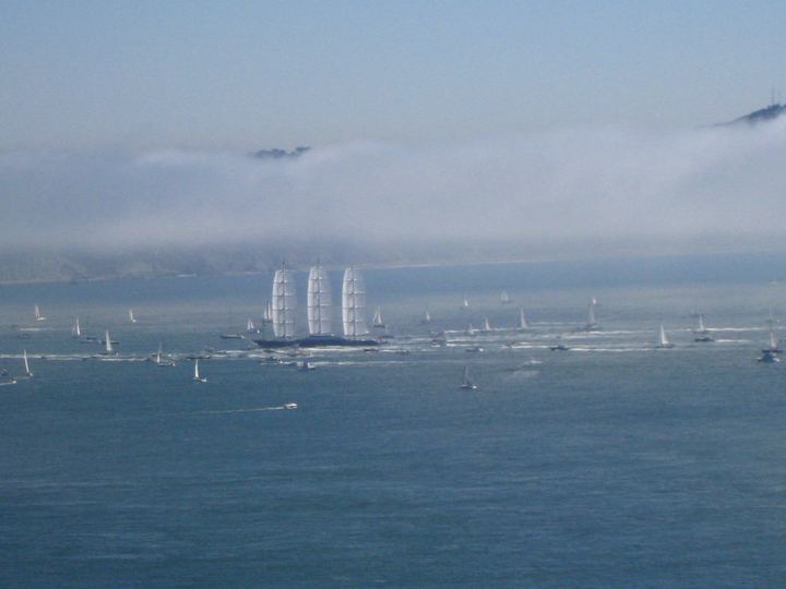 The Maltese Falcon under full sail on a bay, with fog rolling over the hills behind