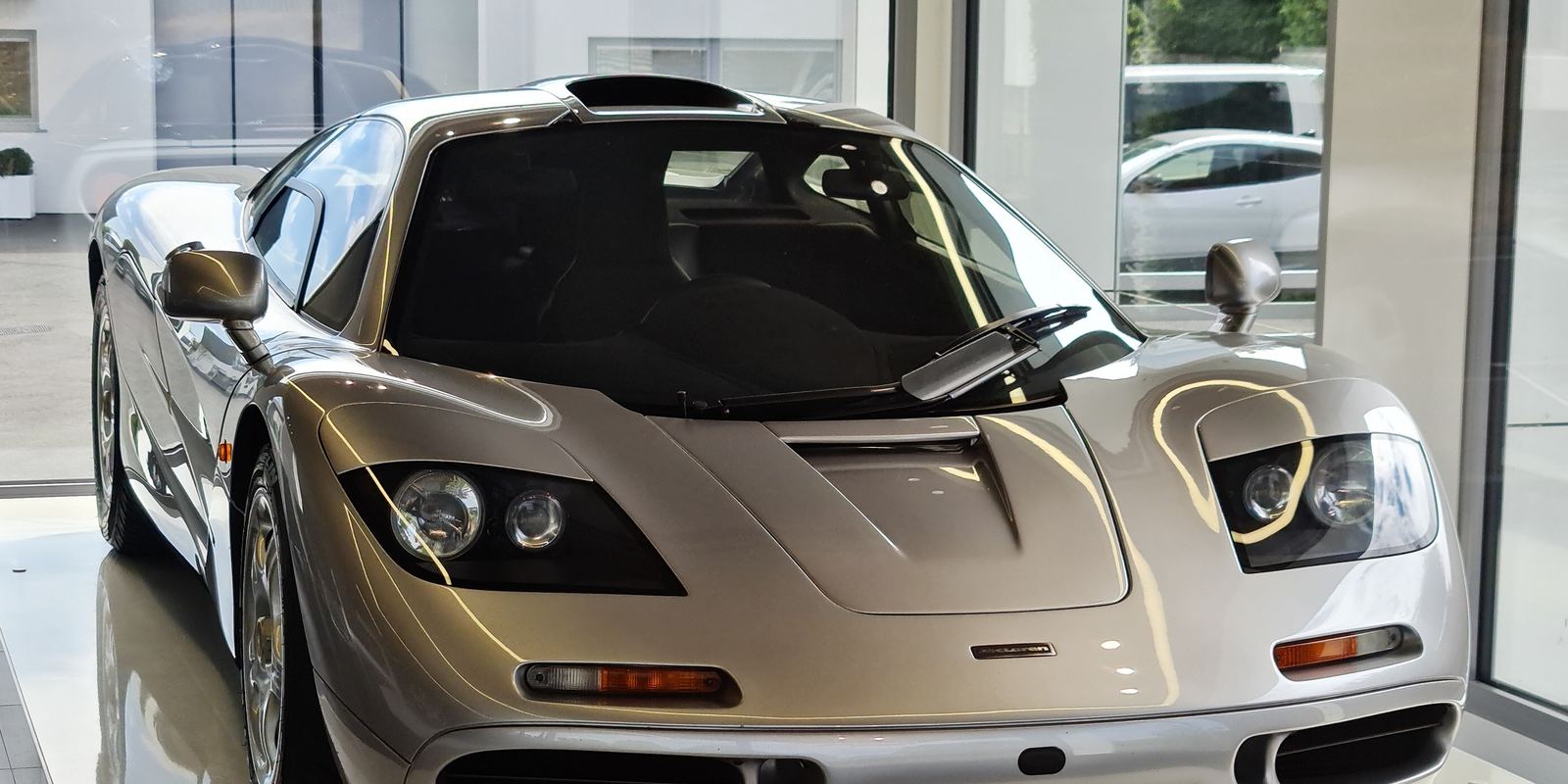 A silver McLaren F1 road car shown from the front in a showroom