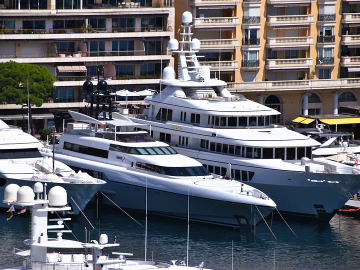 Large white motor yachts moored side by side in Port Hercules, Monaco, with apartment buildings behind