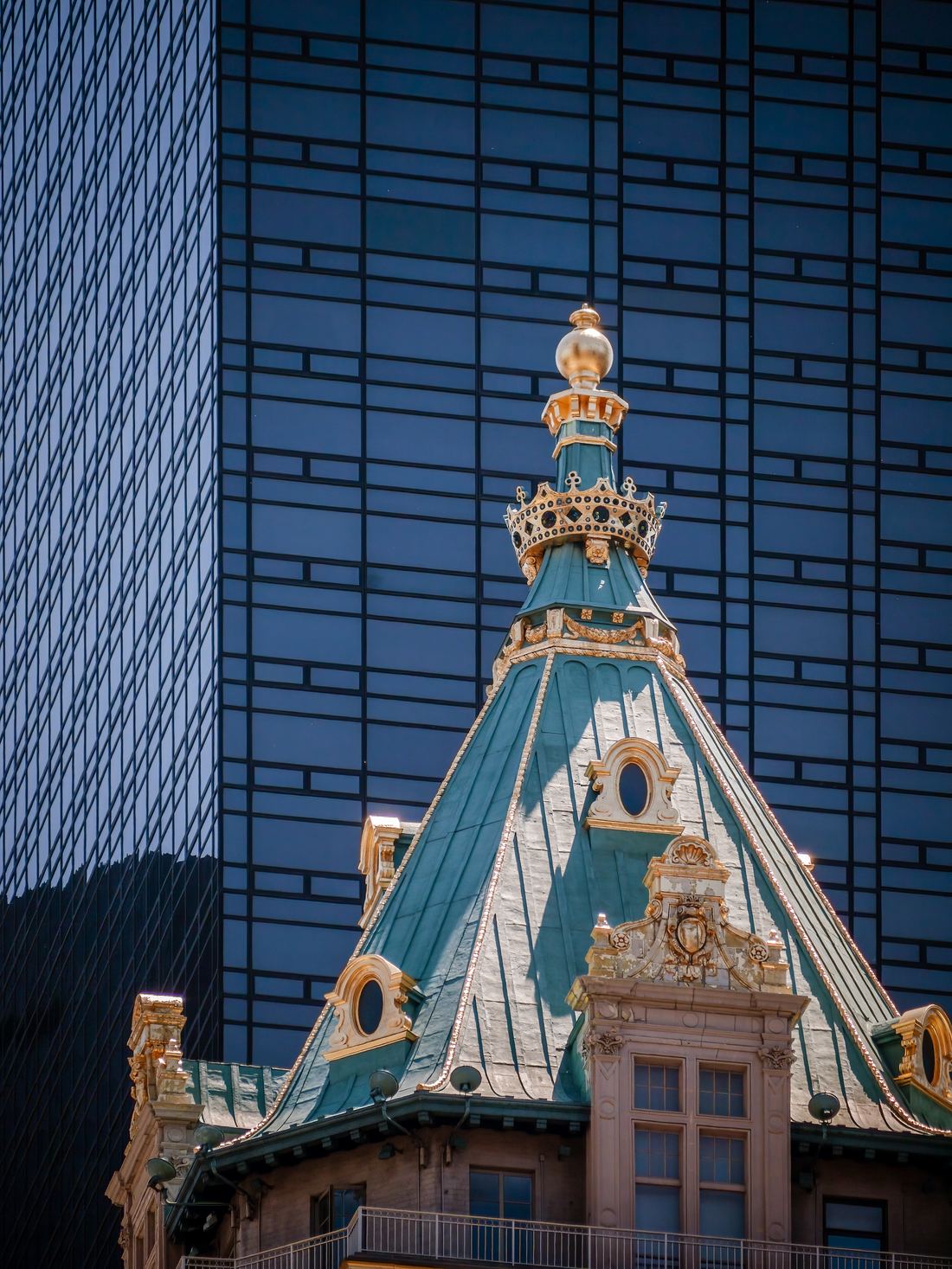 The green copper roof and ornate turret of The Plaza hotel against a modern glass tower