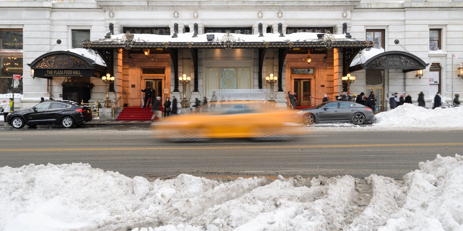 The arched entrance of The Plaza hotel in New York in winter with a yellow taxi blurring past